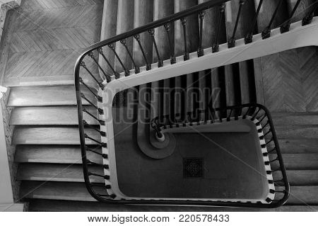 Winding interior staircase with bannister rails in a rectangular stairwell viewed from the top looking down to the ground floor