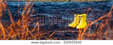 Yellow rubber boots in black rural mud road. Spring and autumn weather concept.