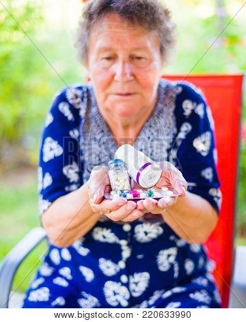 Closeup of senior woman holding her expensive drugs and being disappointed outdoors.