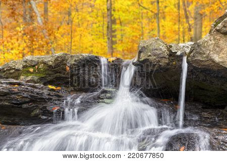 Whitewater splashes over a small cliff with a colorful autumn display above Tailwater Falls, a small waterfall in Owen County, Indiana.