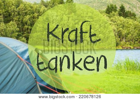 German Text Kraft Tanken Means Relax. Camping Holiday In Norway At Lake Or River. Green Grass And Forest In Background. Tent In The Front