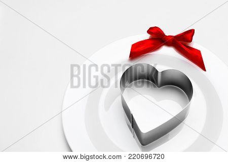 Metal heart mold on white plate with red ribbon bow.Background for valentine's day.Minimalism.Copy space