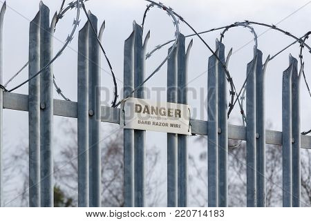 Galvanised steel spikes on top of a security gate or fence topped with barbed razor wire with a danger notice