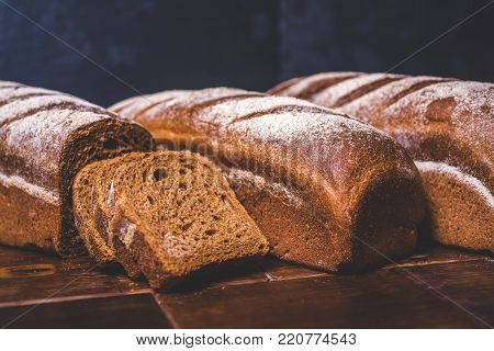Loaves of rye bread lie next to each other. Sliced pieces of bread lie near the loaf. Bread is strewn with white flour.