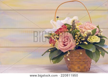 A flower basket with frangrant lilies, red and pink roses against light colored wooden background. Space for a text or image. St. Valentine's, anniversary, wedding concept.