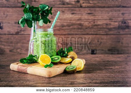 Delicious kiwi smoothie with mint in mason jar on table against dark wooden background.