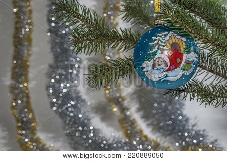 Christmas blue ball with the dog on its side on a blurred background of spruce and colorful tinsel.
