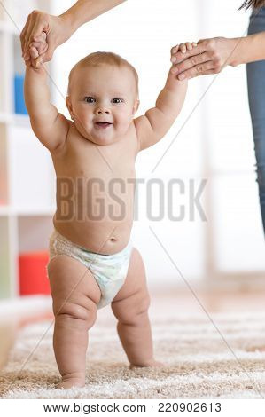 Cute baby taking first steps holding mother hands