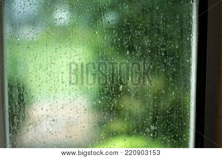 Abstract blurred of wet window pane with raindrops and greenery background on overcast rainy day