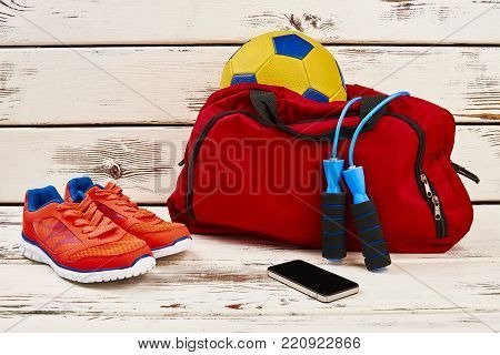 Sneakers, mobile phone and equipment. Jumping rope and soccer ball in gym bag. Locker room concept.