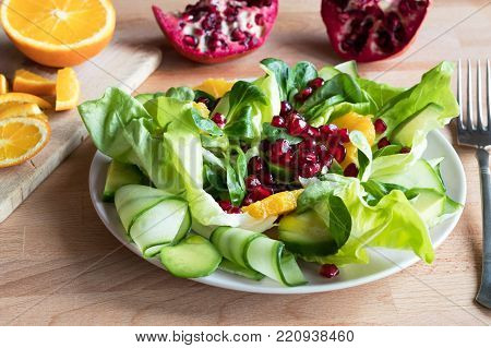Vegetable salad with lettuce, corn salad, cucumber, avocado, orange, and pomegranate seeds.