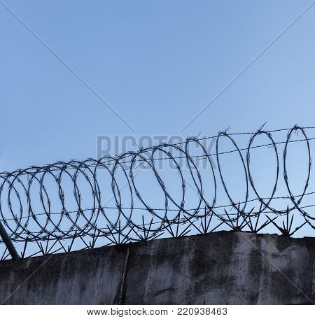 Barbed wire spiral on top of rough high stone wall on the sky background Stock photo