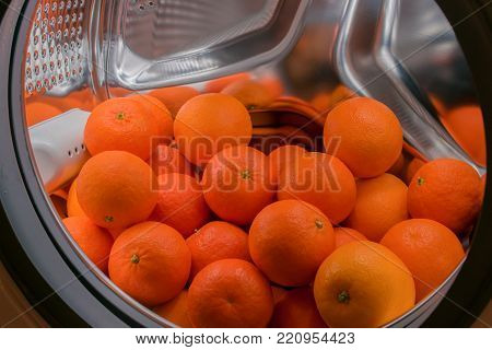 a lot of fresh tangerines lie in the drum of a washing machine