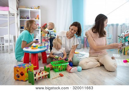 Nursery Babies Playing Toys Together With Moms In Creche Or Children Club