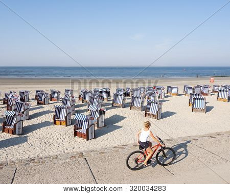 Norderney, Germany, 25 August 2019: Woman On Bicycle Passes Beach Korbs On The Island Of Norderney I