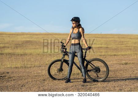 Girl On A Mountain Bike On Offroad, Beautiful Portrait Of A Cyclist At Sunset, Fitness Girl Rides A 