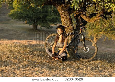 Girl On A Mountain Bike On Offroad, Beautiful Portrait Of A Cyclist At Sunset, Fitness Girl Rides A 
