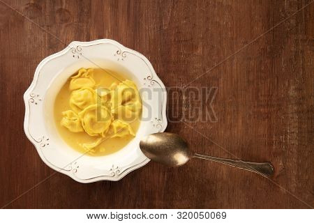 Tortellini Served With Broth, Overhead Shot On A Dark Rustic Wooden Background With A Place For Text