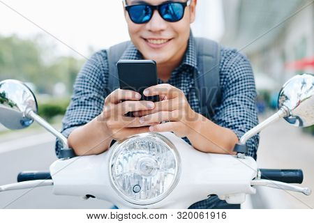 Happy Young Asian Man In Sunglasses Sitting On Scooter And Checking Text Messages And Notifications 