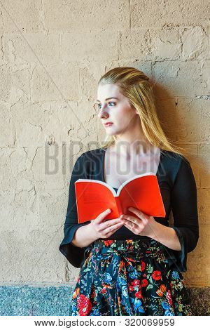 American Teenage Girl With Long Blonde Hair, White Skin, Reading Book Outside In New York, Wearing B