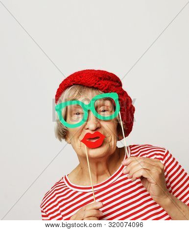 lifestyle, people and party concept: funny grandmother wearing red clothes holding falce glasses