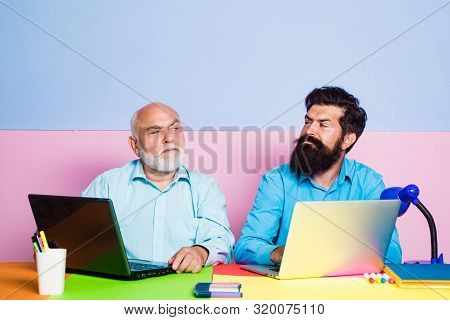 Two Businessmen Working At Workplace. Businessmen Using Laptop At Work. Two Different Generations Ag