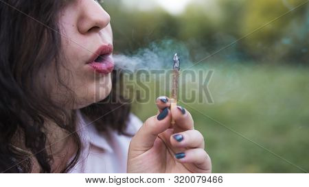 Girl Smoking Medical Marijuana Joint Outdoors, Close-up. Cannabis Is A Concept Of Herbal Medicine.