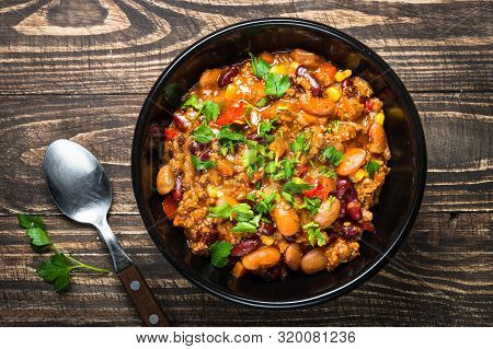 Chili Con Carne With Meat, Beans And Vegetables With Herbs On Wooden Table. Traditional Mexican Food