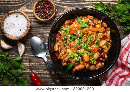 Chili Con Carne With Meat, Beans And Vegetables With Herbs On Wooden Table. Traditional Mexican Food