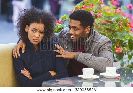 Couple Fighting. Cheerful Afro Guy Trying To Cheer Up His Angry Girlfriend, Cafe Interior