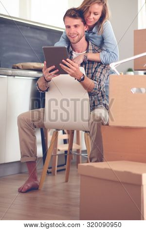Young couple moving in new home.Sitting and relaxing after unpacking.Looking something on laptop. Young couple