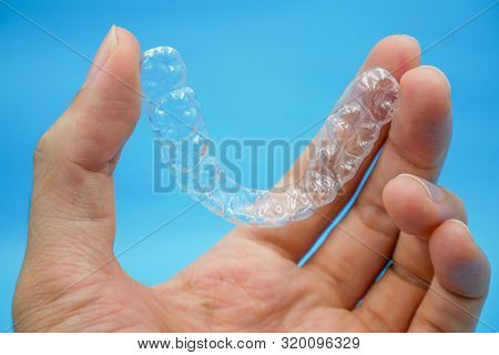 Hand Holding Clear Plastic Retainer Teeth That Isolated On Blue Sky Background. It's An Equipment Fo