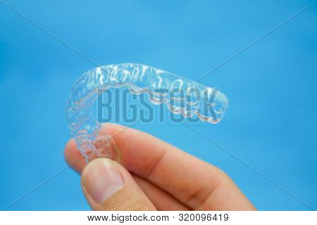 Hand Holding Clear Plastic Retainer Teeth That Isolated On Blue Sky Background. It's An Equipment Fo