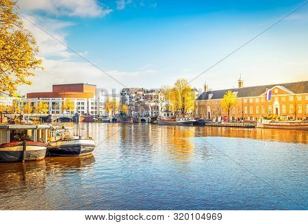 Embankments Of Amstel Canal With Traditional Boats And Houses In Amsterdam, Holand At Fall
