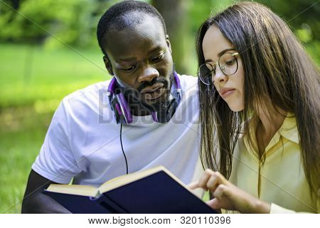 African-american Lad Reading Book With Fellow Asian Female Student