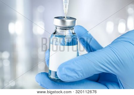 Healthcare concept with a hand in blue medical gloves holding a vaccine vial with blue liquid and black white label
