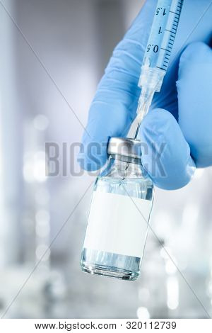 Healthcare concept with a hand in blue medical gloves holding a vaccine vial with blue liquid and black white label