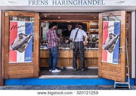 Amsterdam, The Netherlands - July 1, 2019: Two Clients Buying Herring As Red-white-blue Fast Food In