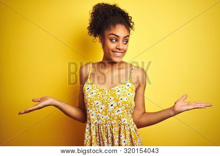 African american woman wearing casual floral dress standing over isolated yellow background smiling showing both hands open palms, presenting and advertising comparison and balance