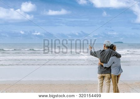 Asian Senior Couple Or Elderly People Walking And Siting At The Beach On Their Weekend Vacation Holi