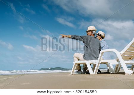 Asian Senior Couple Or Elderly People Walking And Siting At The Beach On Their Weekend Vacation Holi