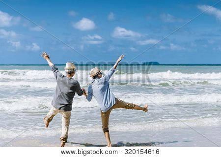 Asian Senior Couple Or Elderly People Walking And Siting At The Beach On Their Weekend Vacation Holi