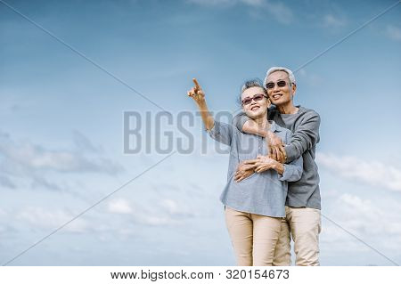 Asian Senior Couple Or Elderly People Walking And Siting At The Beach On Their Weekend Vacation Holi