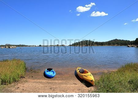Blue And Yellow Kayaks Are Parked On The Sandy Beach On A Sunny Day On Dowdy Lake, Colorado.