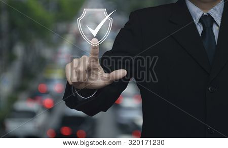 Businessman Pressing Security Shield With Check Mark Icon Over Blur Of Rush Hour With Cars And Road 
