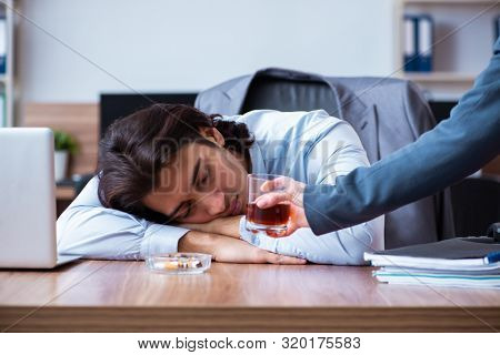 Male employee drinking alcohol and smoking cigarettes at workpla