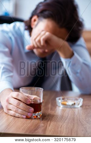 Male employee drinking alcohol and smoking cigarettes at workpla