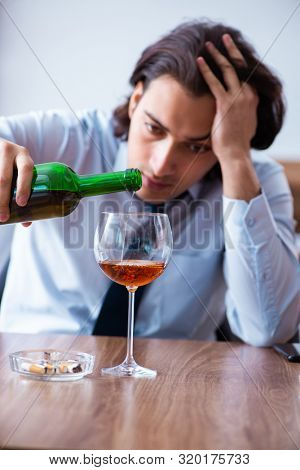 Male employee drinking alcohol and smoking cigarettes at workpla
