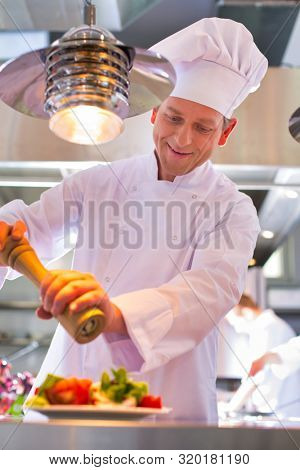 Mature chef using peppermill on salad in plate at restaurant