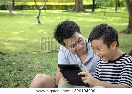 Father And Son Using A Tablet And Smiling Happy While Spending Time Together At Patk , Happy Family 